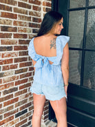 Model wearing the Blue Gingham Bow Tie Back Top with high-rise denim, highlighting the flirty open back and trendy self-tie bow design.