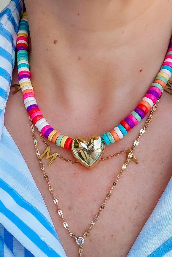Stylish HEY GIRLIE BEADED NECKLACE featuring vibrant beads, a gold heart charm, and a 15" length with 2" extender, perfect for adding glamour to any outfit.