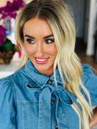 Close-up of the Entro denim dress with bow tie neck, highlighting the button-down design and playful details.