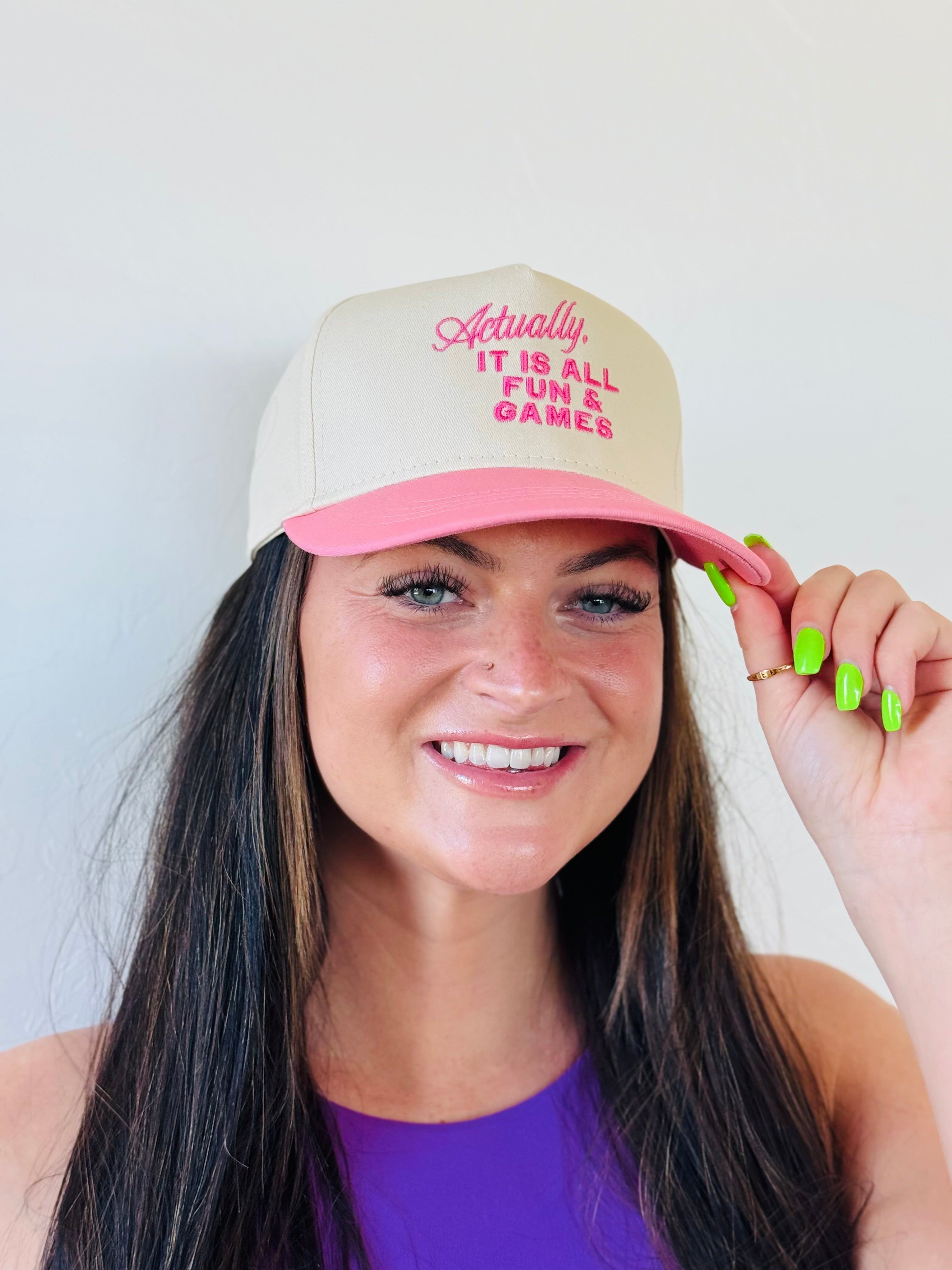 ACTUALLY IT IS ALL FUN & GAMES TRUCKER HAT in pink and natural colors, showcasing its embroidered design perfect for adding a playful touch to any outfit.