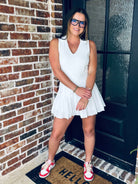 A model showcasing the WHITE V-NECK COLLARED ATHLETIC DRESS with a pleated skirt, built-in shorts, and back zipper, perfect for athletic activities and casual wear.