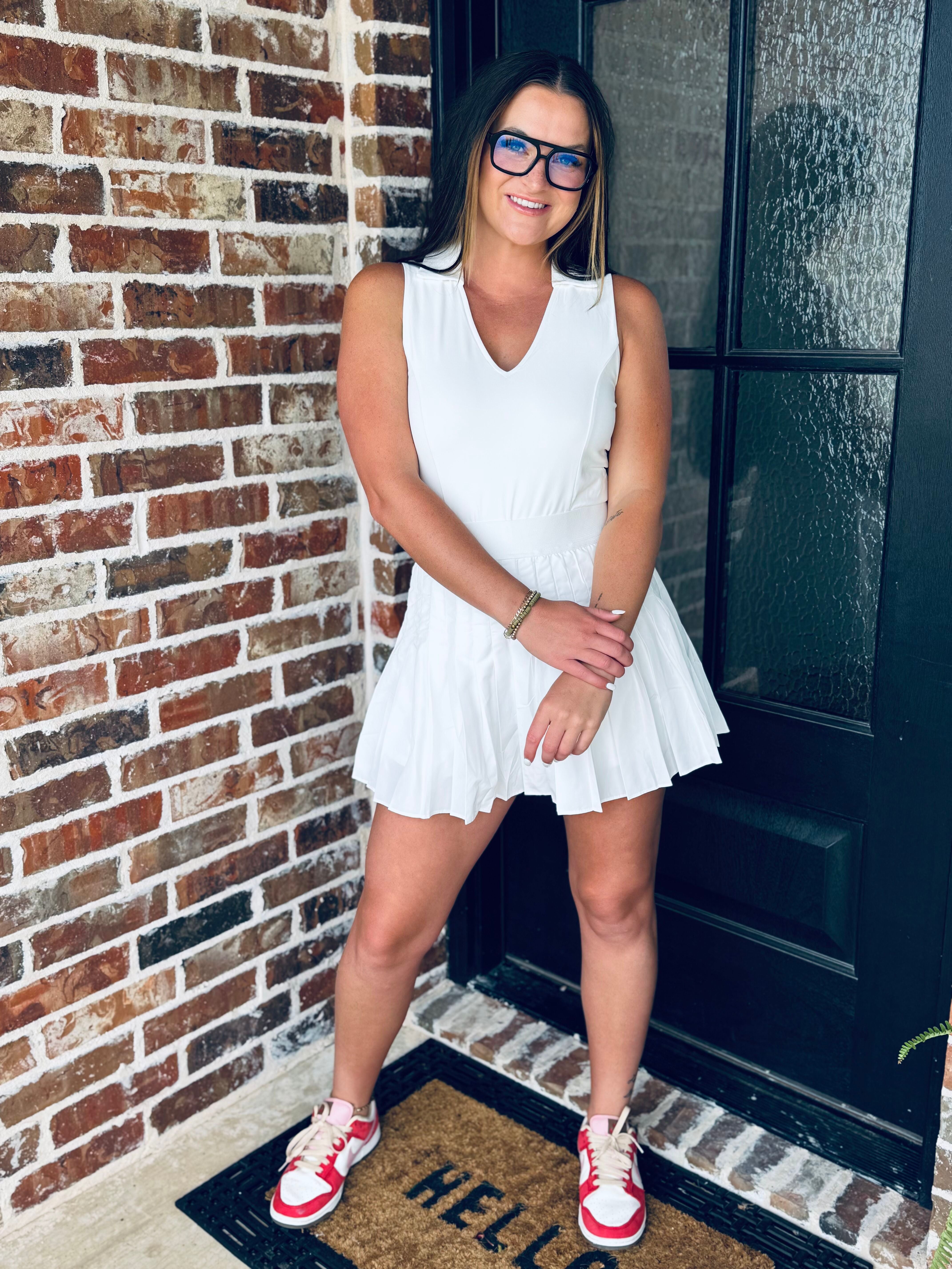 A model showcasing the WHITE V-NECK COLLARED ATHLETIC DRESS with a pleated skirt, built-in shorts, and back zipper, perfect for athletic activities and casual wear.