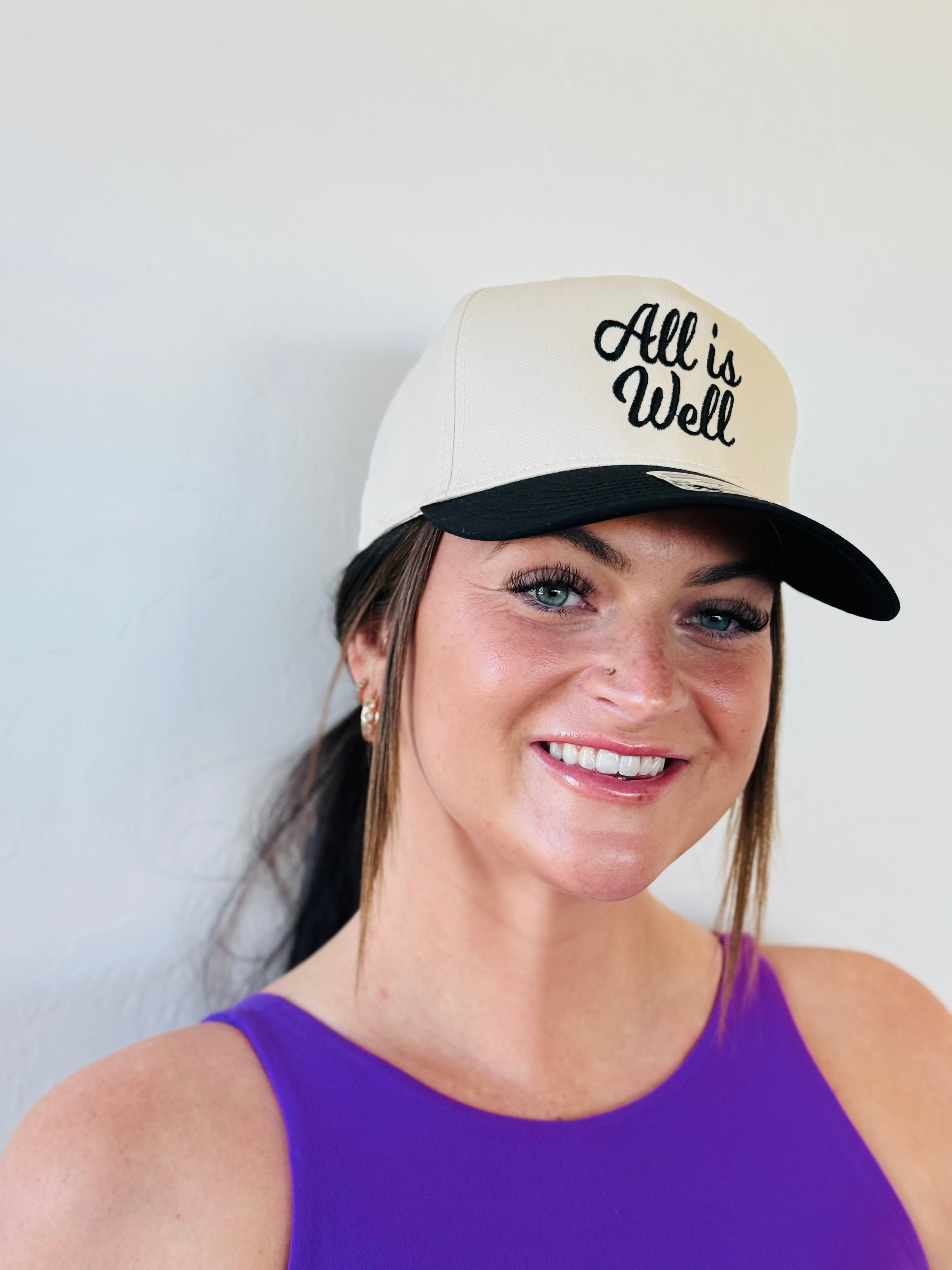 ALL IS WELL EMBROIDERED TRUCKER HAT showcasing bold black embroidery against a natural color background, perfect for outdoor style.